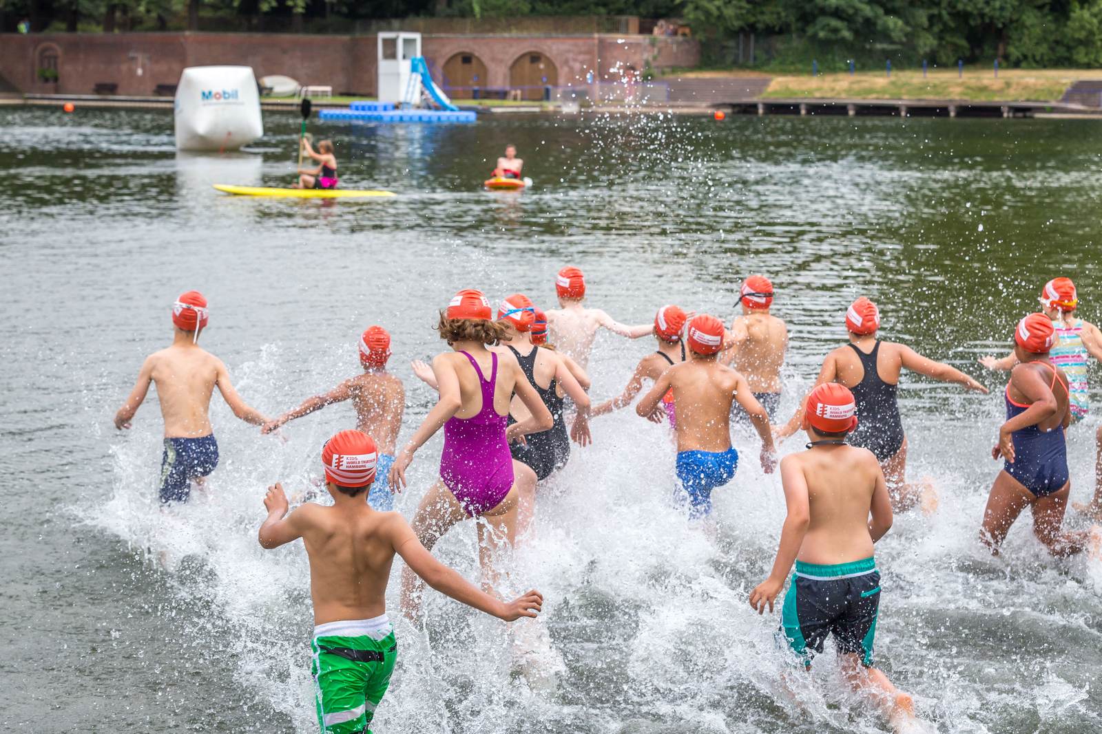 Zahlreiche Kinder mit roten Badekappen laufen nebeneinander in einen See — der Schwimmstart des Kids Triathlon Hamburg